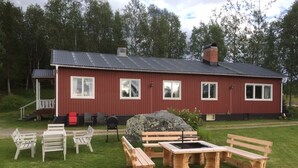 Een rood gebouw met een metalen dak, een stenen open haard, en een houten tafel met bankjes op de voorgrond.