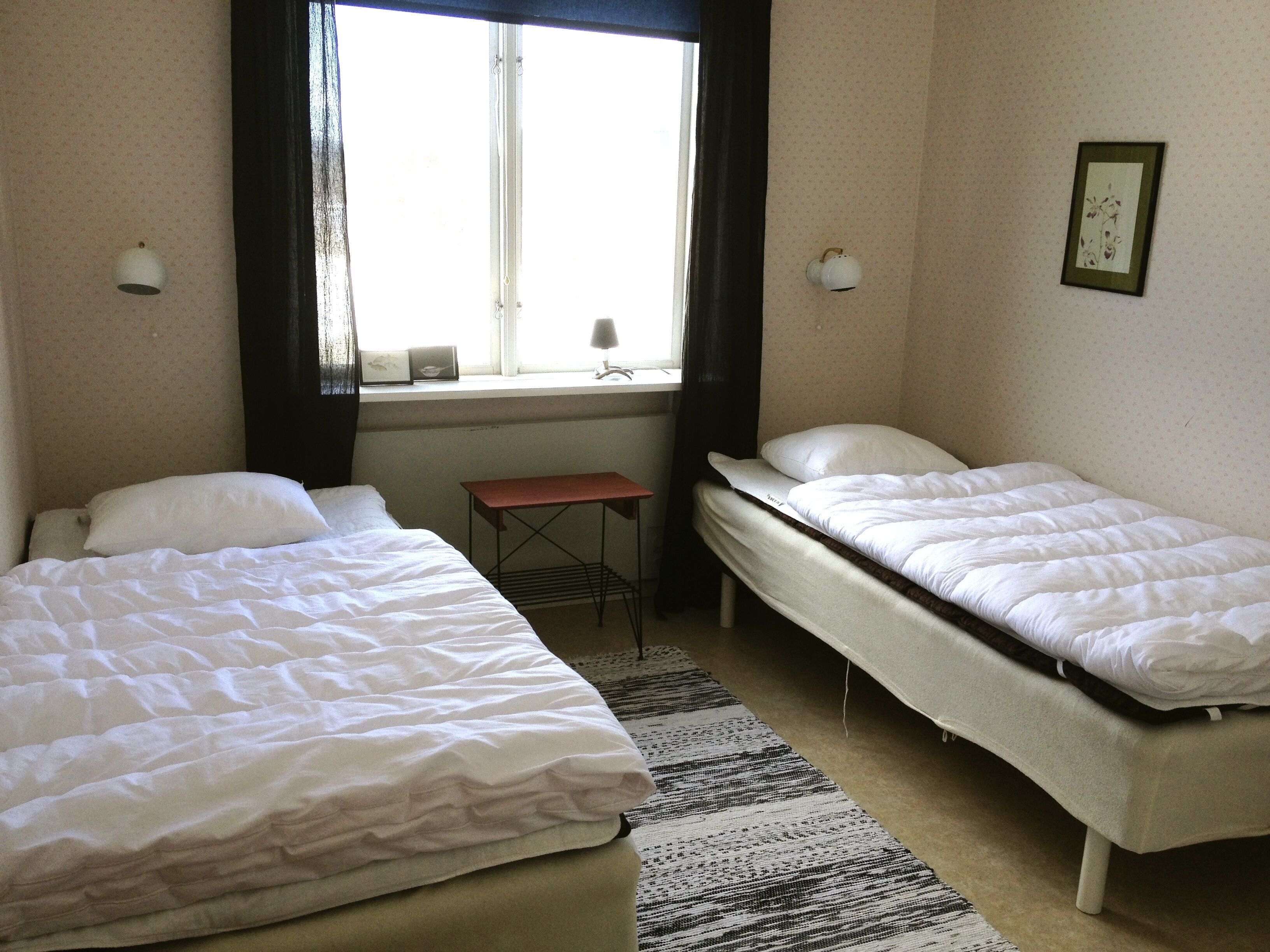 A hotel room with two single beds, a small table, and a window with curtains.