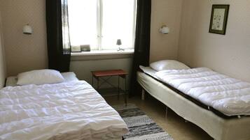 A hotel room with two single beds, a small table, and a window with curtains.