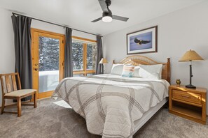 A bedroom with a bed, a chair, a nightstand, a lamp, a ceiling fan, and a window with curtains. - >100 Yards to Slopes + Private Hot Tub w/ Gondola Views EZCancel (Steamboat Springs)