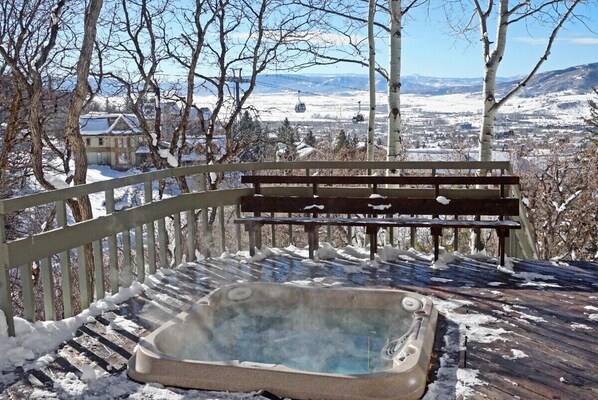 A hot tub on a wooden deck with a bench, surrounded by snow-covered trees and a view of a town and mountains in the background. - >100 Yards to Slopes + Private Hot Tub w/ Gondola Views EZCancel (Steamboat Springs)