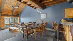 A rustic dining area with a wooden table and chairs, a bar area with stools, and a large window offering a view of snow-covered trees. - Less Than 100 Yards to Slopes + Private Hot Tub w/ Gondola Views (Steamboat Springs)