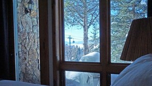 A room with a stone wall, a window with a view of a snowy landscape and a chair outside. - Less Than 100 Yards to Slopes + Private Hot Tub w/ Gondola Views (Steamboat Springs)