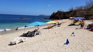 A beach with sun loungers, umbrellas, and a rocky cliff in the background. - Gringo Paradise, a perfect Costa Rican get away! (Potrero)