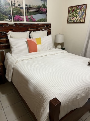 A neatly made bed with striped bedding, a wooden headboard, and a bedside lamp.