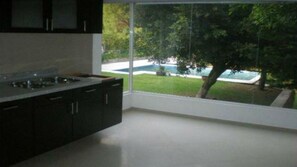 Una cocina moderna con armarios oscuros y un amplio ventanal con vistas a una piscina y zonas verdes.
