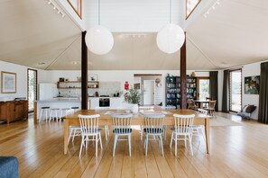 A spacious living area with a wooden dining table and chairs, a kitchen in the background, and a large bookshelf. - Abercorn - one of Stayz’s 2025 Holiday Homes of the Year (Buckaroo)
