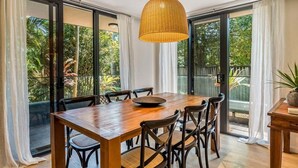 Ein Essbereich mit Holztisch und Stühlen, großen Fenstern mit Vorhängen und einer hängenden Leuchte.