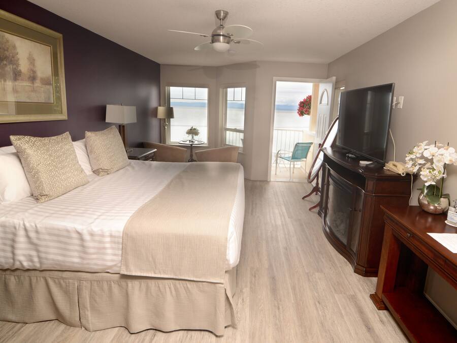 A hotel room with a large bed, a TV, a desk, and a view of the sea.