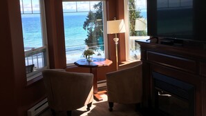 Una sala de estar con chimenea, televisor y ventanas amplias con vista al océano.