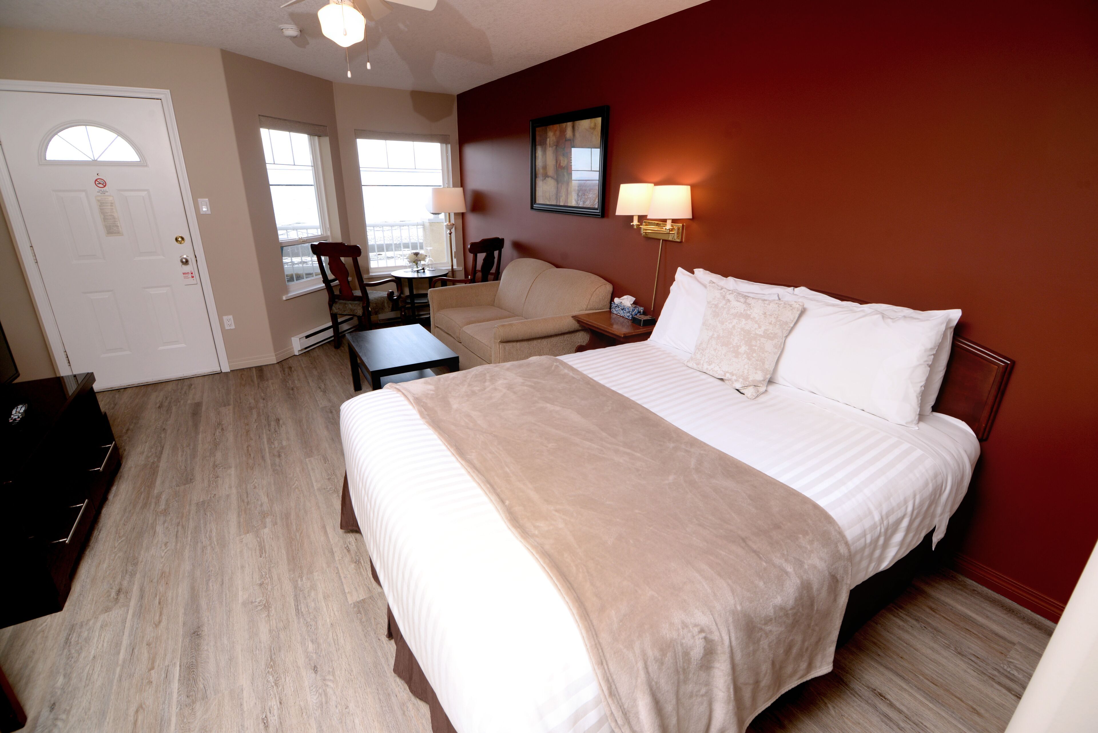 A hotel room with a large bed, a desk, a chair, and a small table.