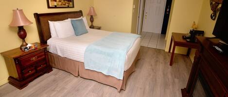 Un dormitorio con cama, cómoda de madera, mesitas de noche y televisor.