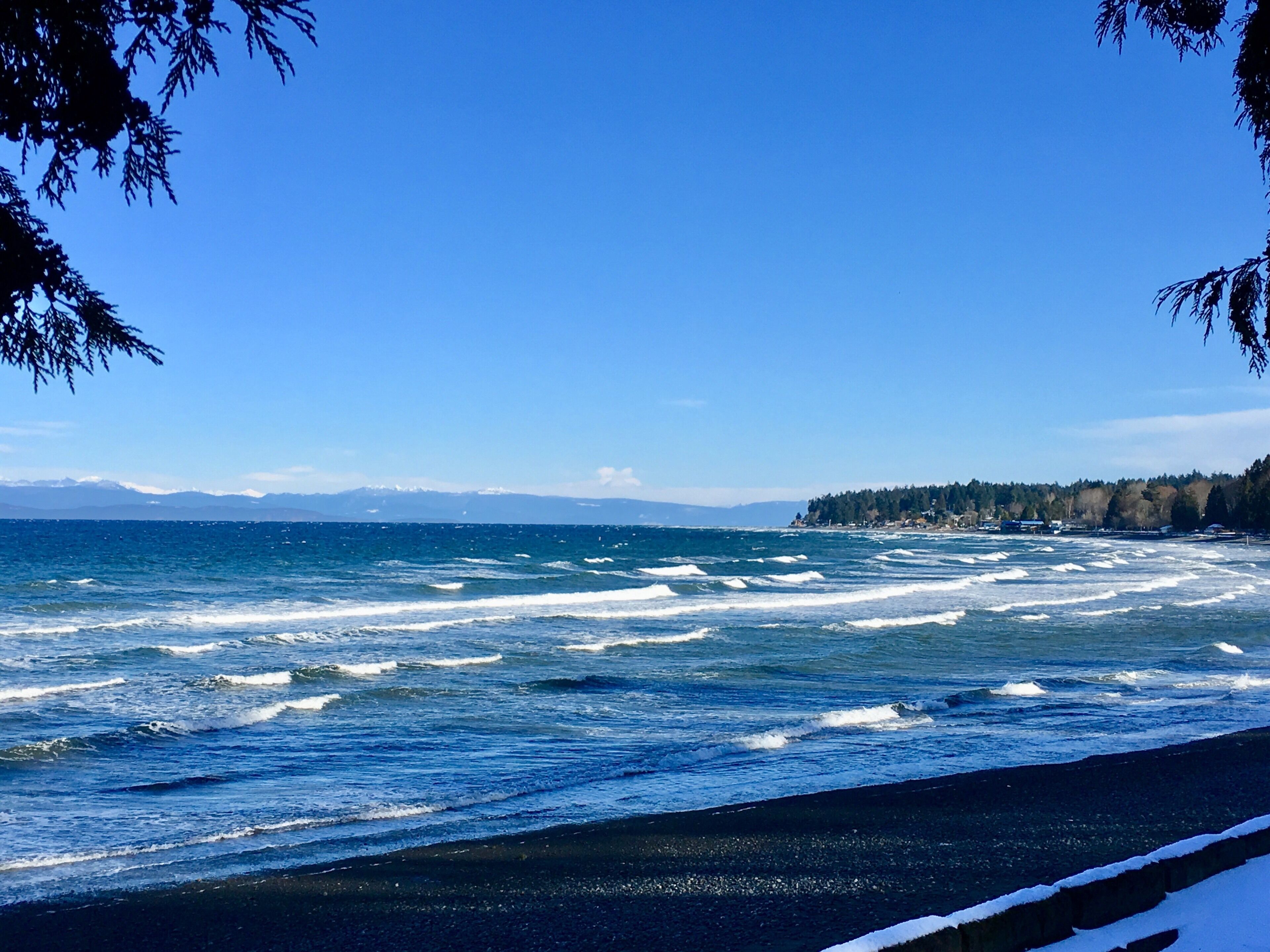 Une vue sur la côte, avec des vagues qui s’écrasent sur un rivage rocheux, un ciel dégagé et des montagnes lointaines.
