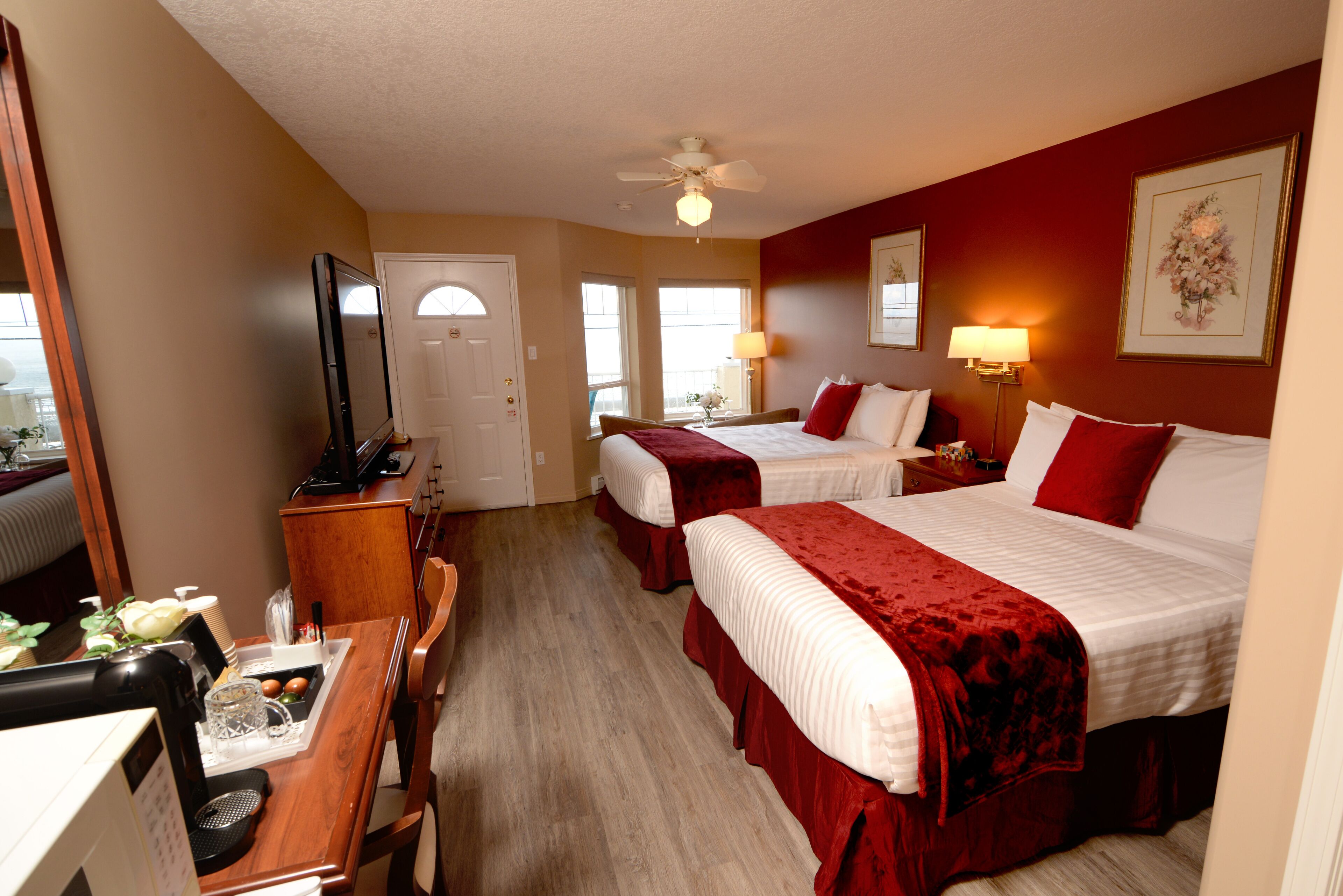 A hotel room with two beds, a desk with a computer, a television, and a dining area with a table and chairs.