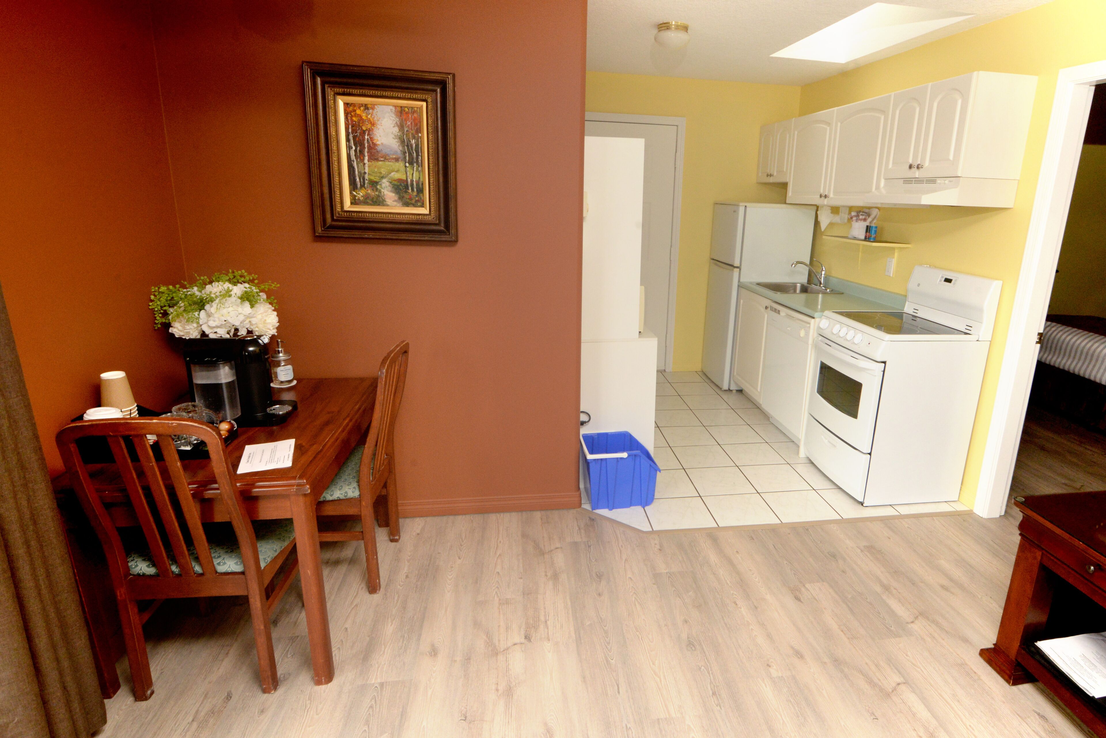 Una cocina compacta con electrodomésticos blancos, un comedor con mesa y sillas de madera, y un cuadro en la pared.