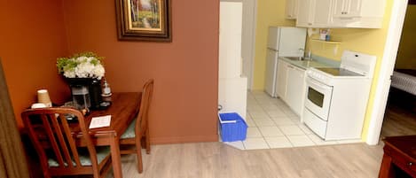 Una cocina compacta con electrodomésticos blancos, un comedor con mesa y sillas de madera, y un cuadro en la pared.