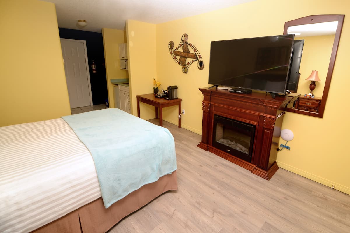 A hotel room with a bed, a television, a fireplace, and a small table with a lamp.