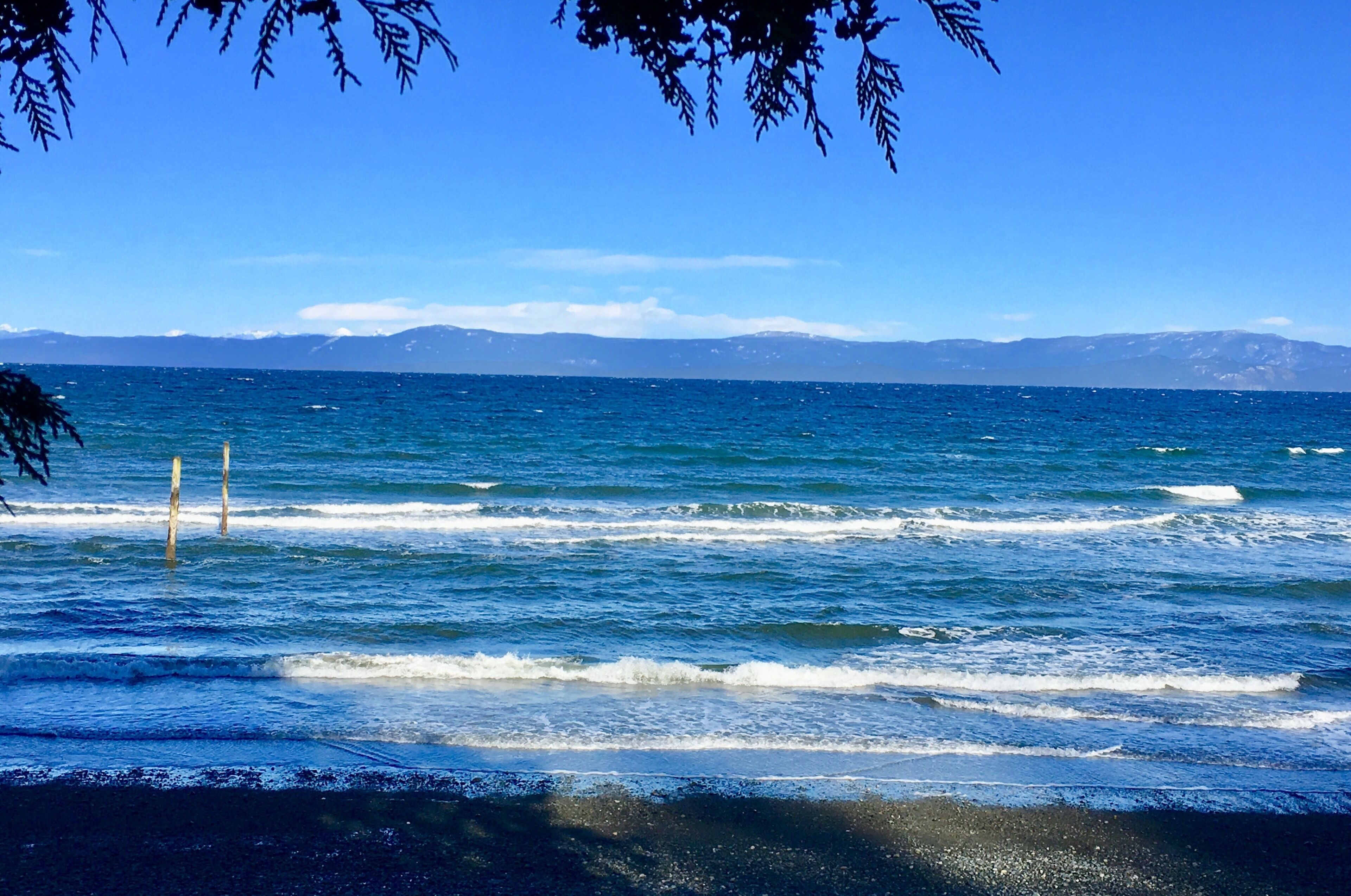 A coastal view with waves, a clear sky, and distant mountains.