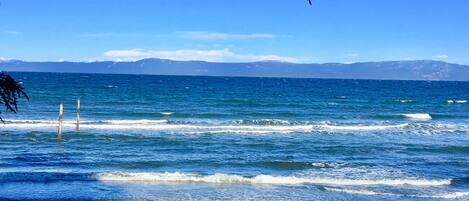 A coastal view with waves, a clear sky, and distant mountains.