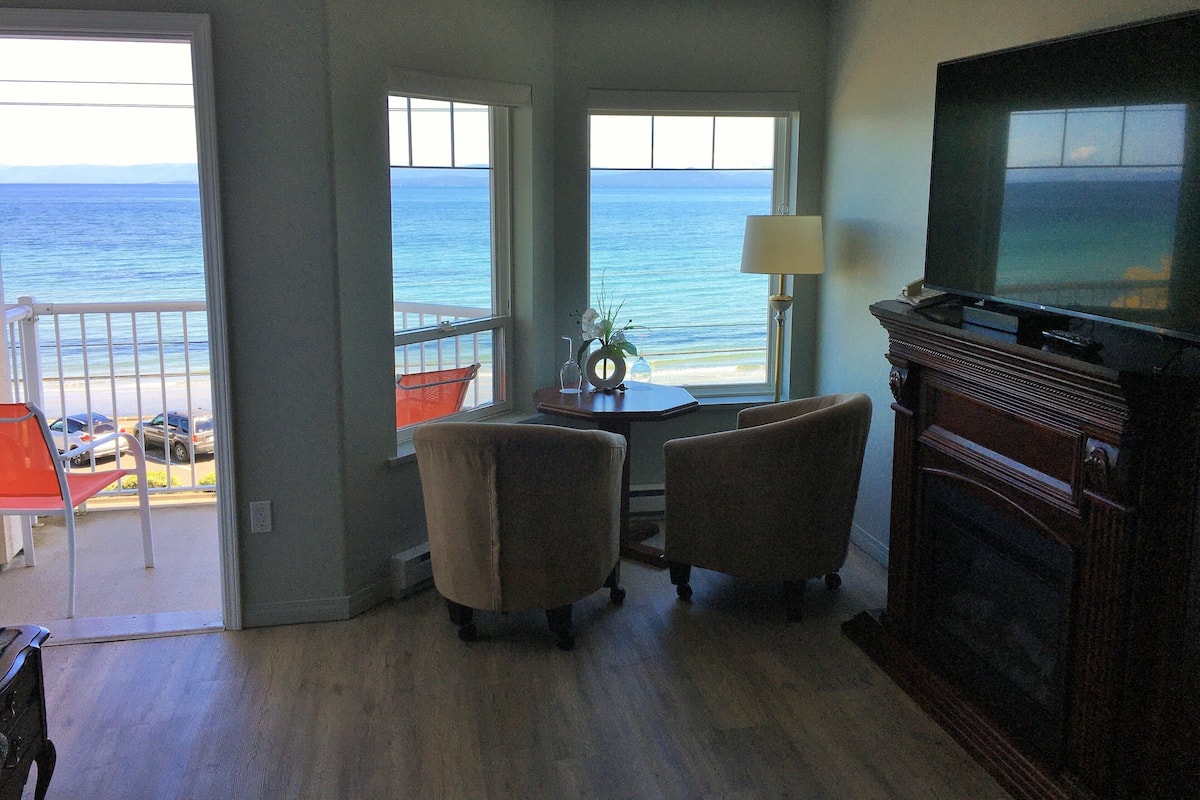A living room with a view of the ocean, a fireplace, and a television.