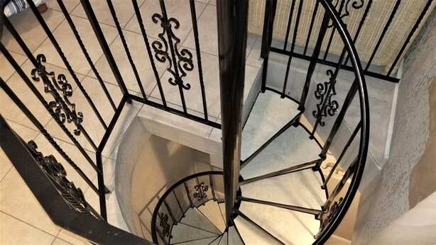 A spiral staircase with ornate black metal railings and white steps. - The Octagon at Capricorn (South Padre Island)