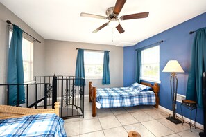 A room with two beds, a ceiling fan, and a window with curtains.