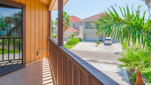 A balcony with a wooden railing overlooking a street with houses and palm trees. - The Octagon at Capricorn (South Padre Island)