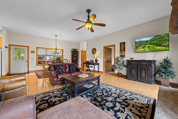 A spacious living room with a leather sofa, a coffee table, and a television mounted on the wall.