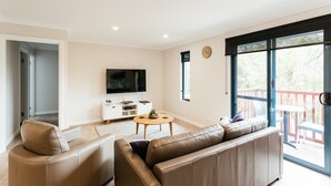 Un salon moderne comprenant un canapé, une table basse, un téléviseur et un balcon aménagé avec du mobilier d’extérieur.