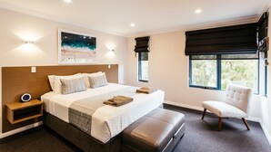 Une chambre d’hôtel moderne avec un grand lit, une table de chevet avec une horloge, une chaise et une fenêtre donnant sur des arbres.