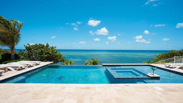 Ein Pool mit Blick auf das Meer, umgeben von Liegestühlen und Palmen.