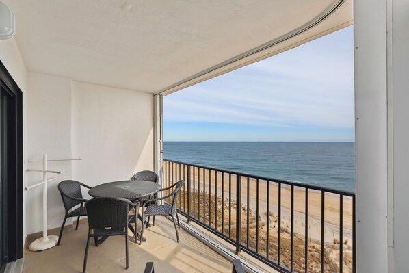 Un balcón con mesa y sillas, una lámpara de pie blanca y vista a la playa y al océano.
