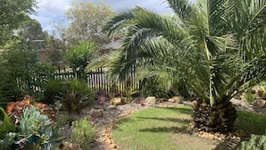A well-maintained garden with various plants, a palm tree, and a wooden fence. - Private , tranquil cosy retreat with massage chair-l (Melbourne)