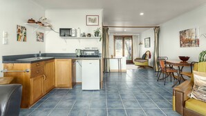 Una cocina moderna con armarios de madera, microondas integrado y un refrigerador pequeño. Hay una zona de comedor con mesa y sillas, y una sala de estar con sofá y mesita de centro.