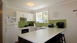 A compact kitchen with white cabinets, a green backsplash, a window, and basic appliances. - Wrights Beach Bungalow by Book Jervis Bay - Walking Distance TO THE Water (Wrights Beach)
