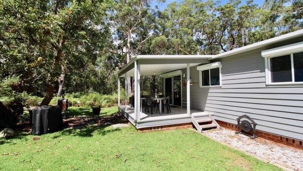 A single-story house with a covered patio area, a small outdoor seating space, and a garden with a lawn and trees. - Wrights Beach Bungalow by Book Jervis Bay - Walking Distance TO THE Water (Wrights Beach)