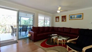 A living room with a red leather sofa, a glass coffee table, and a dining area with a table and chairs. - Wrights Beach Bungalow by Book Jervis Bay - Walking Distance TO THE Water (Wrights Beach)