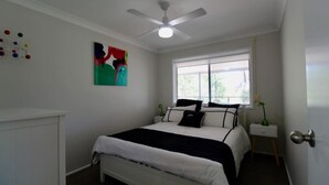 A bedroom with a bed, a ceiling fan, a window, and a wall art piece. - Wrights Beach Bungalow by Book Jervis Bay - Walking Distance TO THE Water (Wrights Beach)