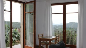 A room with a sliding glass door leading to a balcony with a view of greenery and mountains. There is a wooden table with chairs and a dark-colored sofa. - Lovely greenery detached house with inground private swimming pool.  Large garde (Tresana)
