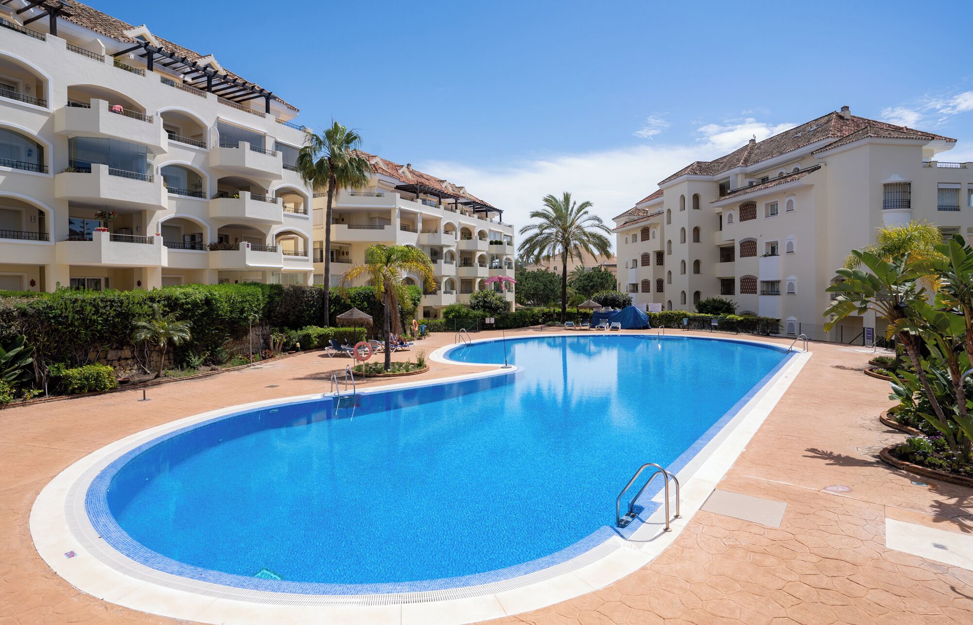 A large swimming pool with a curved edge, surrounded by a paved walkway.