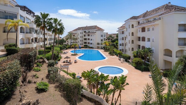 Un resort con piscina central, rodeado de palmeras y edificios de varios pisos con balcones.