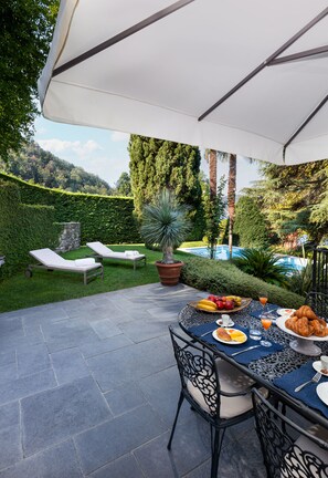 Une terrasse extérieure avec une table préparée pour le petit-déjeuner, des chaises longues et une piscine en arrière-plan.