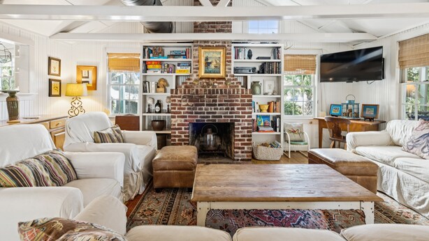 A living room with a brick fireplace, white furniture, and a television mounted on the wall. - Quaint & Charming 2nd Row Beach House - Large Screened Porch - Steps to the Beach (Folly Beach)