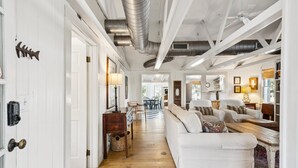 A spacious living room with a white sofa, wooden flooring, and a ceiling with exposed beams and ductwork. - Quaint & Charming 2nd Row Beach House - Large Screened Porch - Steps to the Beach (Folly Beach)