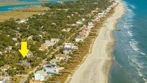 A coastal residential area with houses along the beach, a lighthouse in the distance, and a yellow arrow pointing to a specific house. - Quaint & Charming 2nd Row Beach House - Large Screened Porch - Steps to the Beach (Folly Beach)