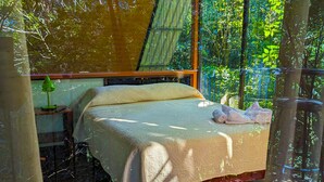 Une chambre à coucher avec un lit, une table de chevet et une fenêtre donnant sur un espace verdoyant.