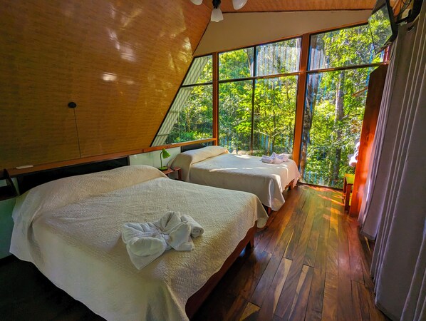 A room with two beds, a wooden ceiling, and large windows overlooking a forest. - Chalet in the mountain #1 (Monteverde)