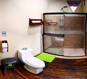 A bathroom with a toilet, a shower stall, a towel rack, and a trash bin. - Chalet in the mountain #1 (Monteverde)