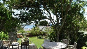 An outdoor patio with a round table and chairs, surrounded by lush greenery and a view of the sea. - Historical Churchtown House - Whole House (Perranuthnoe)