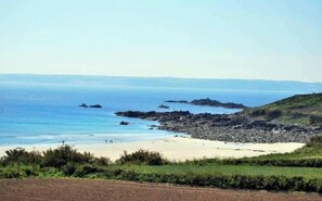 A coastal landscape with a sandy beach, rocky outcrops, and a clear view of the sea.